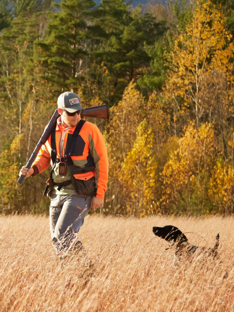 Man and hunting dog walk through a field of wheat together after a long day on the hunt.